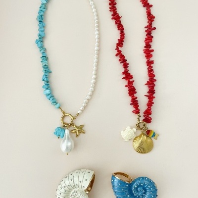 Dois colares coloridos com pedras irregulares e pingentes marítimos, junto com dois anéis em forma de concha, um azul e um branco.