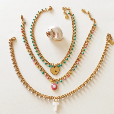 Quatro pulseiras douradas com contas coloridas e pendentes sobre fundo branco, com concha decorativa no centro.