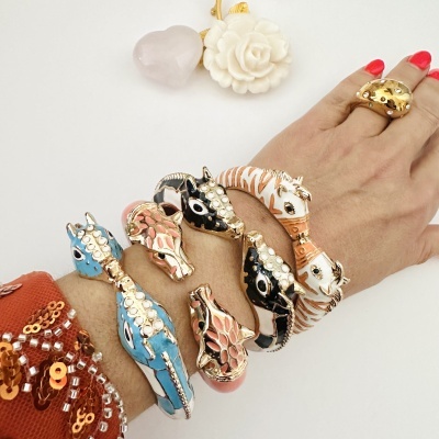 Pulseiras e anel dourados com esmalte decorados com formas de animais numa mão com unhas vermelhas