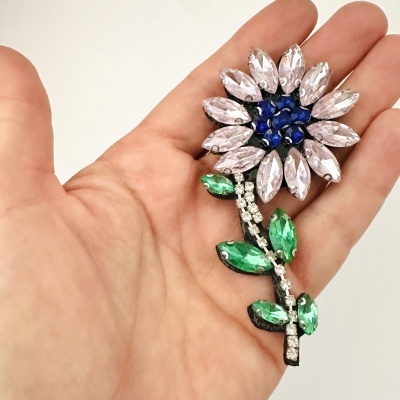 Broche flor com pedras azuis, verdes e lilases faceteadas numa mão