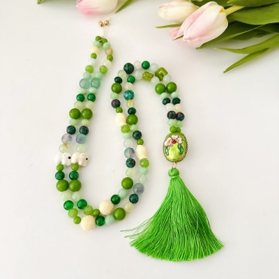 Colar de contas coloridas com pendente floral e tassel verde junto a flores brancas e rosas