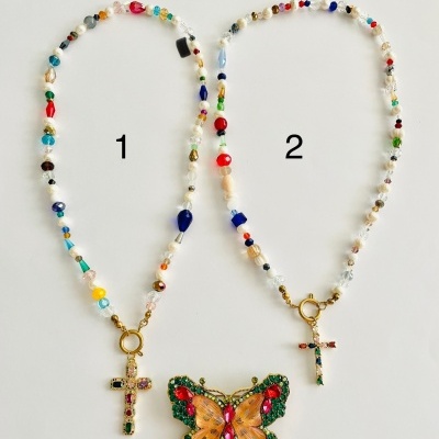 Dois colares com contas coloridas e pingentes, um com cruz de pedras e outro com borboleta colorida.