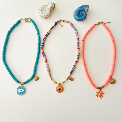 Três colares coloridos com contas e pendentes marinhos sobre fundo branco com conchas decorativas.