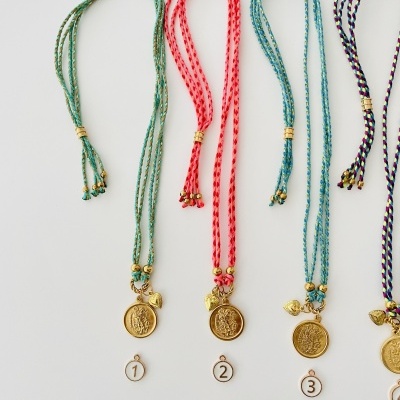 Quatro colares trançados com pingentes dourados e etiquetas numeradas em fundo branco