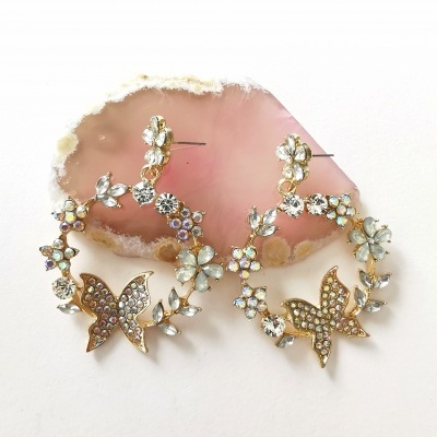 Brincos de argola dourados com pedras e borboletas em exposição