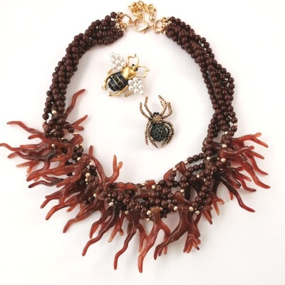 Colar com contas marrons e pendentes vermelhos, dois broches de insetos em fundo branco