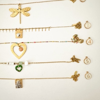 Colares dourados com pendentes variados e etiquetas numeradas em fundo branco
