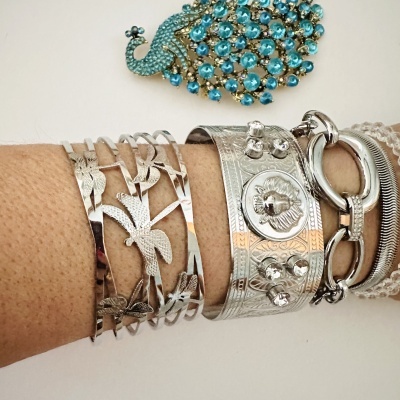 Pulseiras prateadas no pulso com broche de pavão azul