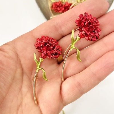 Brincos de flor vermelha com caule dourado e folhas verdes na mão