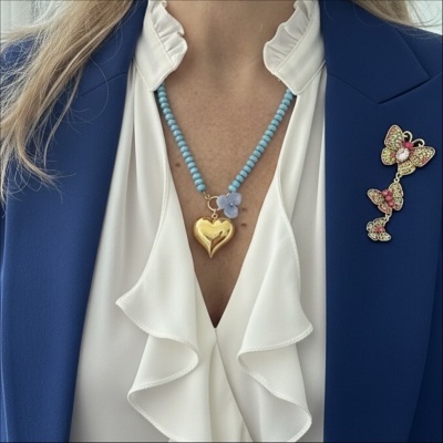Colar com coração dourado e contas azuis usado com blusa branca de folhos e casaco azul com broche de borboletas