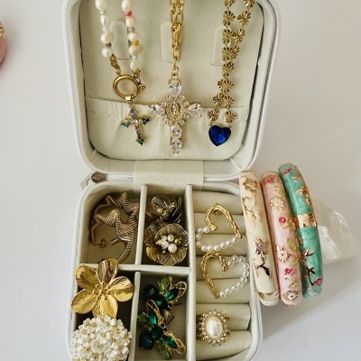 Caixa branca com joias como colares, anéis, brincos e pulseiras coloridas à flor, organizadas em compartimentos.