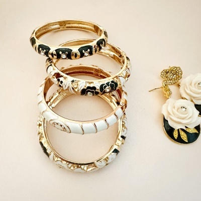 Pulseiras douradas com esmalte preto e branco e brincos dourados com flores brancas