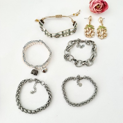 Conjunto de pulseiras e brincos variados sobre fundo branco com uma flor rosa