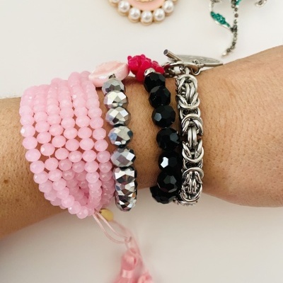 Pulseiras coloridas no pulso com broches decorativos ao fundo