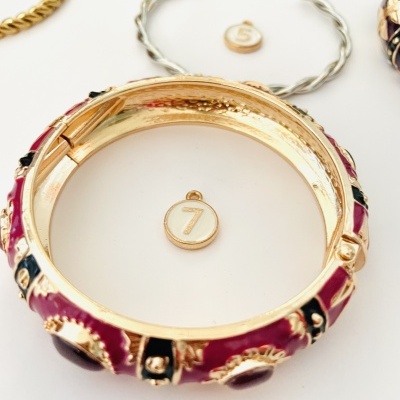 Pulseiras douradas e vermelhas com pingentes numerados em fundo branco