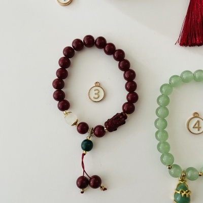 Pulseira de contas vermelhas com pingente verde e detalhes dourados