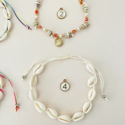 Duas pulseiras artesanais com números, uma com corda laranja e pendente concha, outra com búzios e corda branca.
