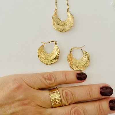 Conjunto de joias douradas com padrão texturizado e mão com unhas pintadas