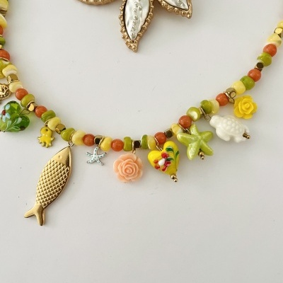 Colar colorido com pendentes variados sobre fundo branco com adorno floral