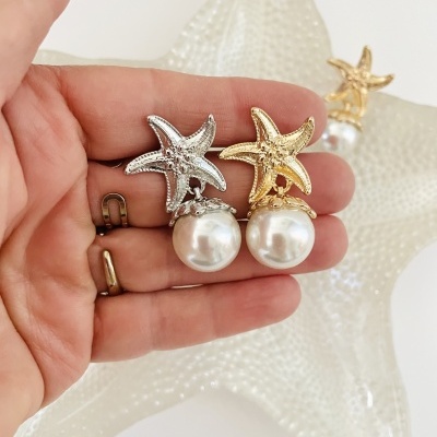 Brincos estrela-do-mar dourado e prateado com pérola, sobre mão e estrela-do-mar decorativa