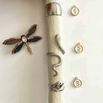 Anéis prateados com designs variados e broche de libélula colorida sobre fundo branco