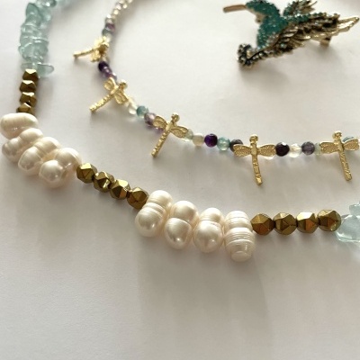 Colares com pérolas, contas douradas e cruzes, e anel com design de pá verde e detalhes dourados