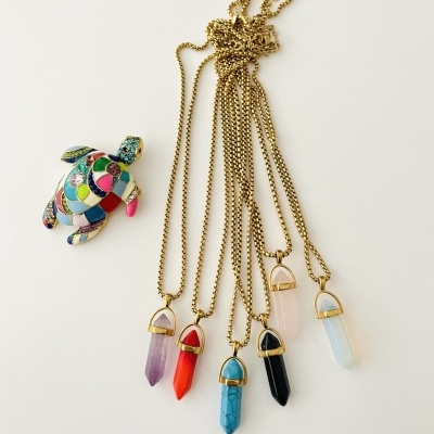 Colares com pendentes de cristal coloridos e broche de tartaruga colorido sobre fundo branco.