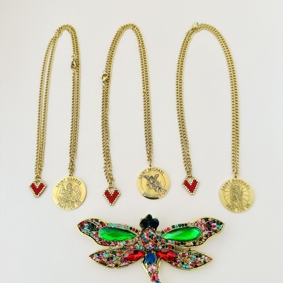 Três colares dourados com medalhões redondos e pingentes em forma de coração vermelho e broche em forma de libélula colorida