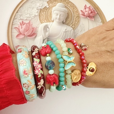 Pulseiras coloridas variadas em pulso com fundo de escultura de Buda branca e rosa.