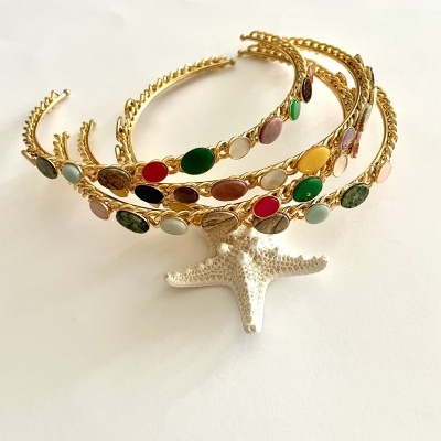 Três tiaras douradas com pedras coloridas empilhadas sobre uma estrela do mar branca