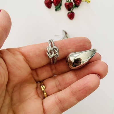 Dois brincos prateados em mão com fundo branco e decoração de frutas vermelhas