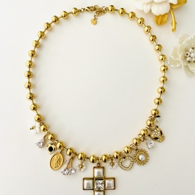 Colar dourado com pendentes variados sobre fundo branco e flores decorativas