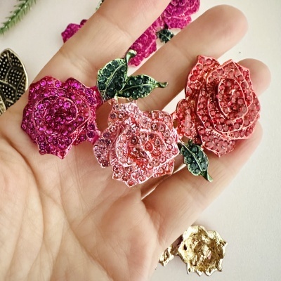 Broche de flores rosas com pedras brilhantes e folhas verdes na palma da mão