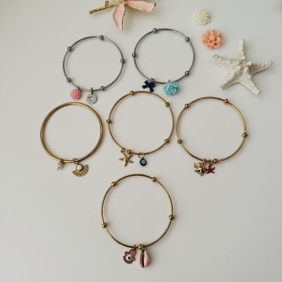 Pulseiras com pendentes em diferentes formas e cores sobre fundo branco com decoração de estrela do mar e flores