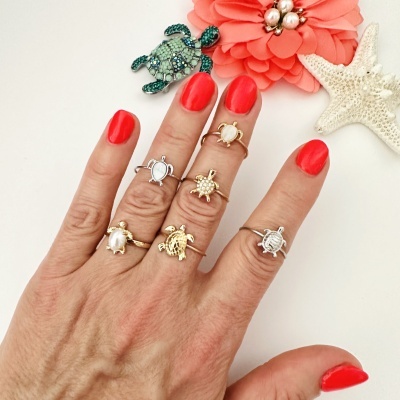 Mão com vários anéis de tartaruga em dourado e prateado com unhas vermelhas e decoração de flor e estrelas-do-mar