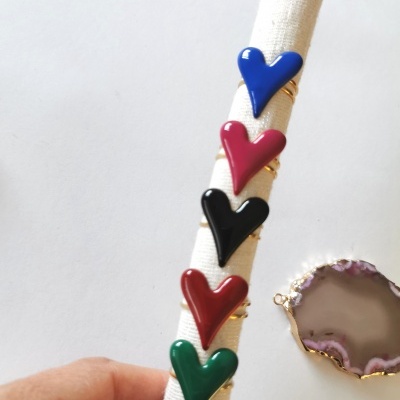 Anéis com corações coloridos exibidos sobre tecido branco, com pedra de ágata ao lado