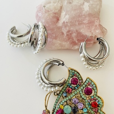 Três pares de brincos prata com pérolas e um broche de borboleta colorido sobre uma pedra rosa