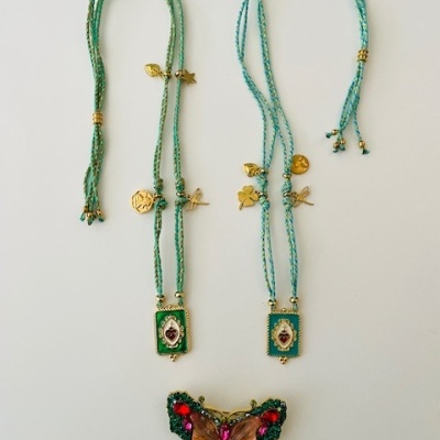 Colares com fio verde e pendentes dourados, com uma borboleta decorativa colorida