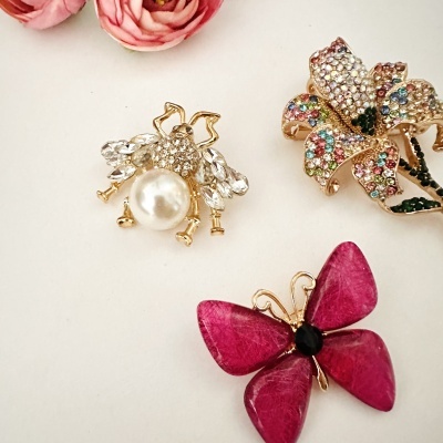 Três broches decorativos em forma de abelha, flor colorida e borboleta rosa
