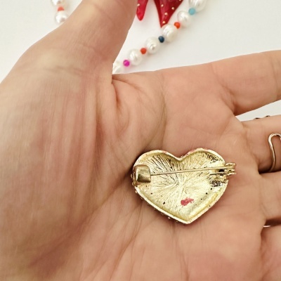 Broche coração dourado com fecho em mão e colar de pérolas ao fundo