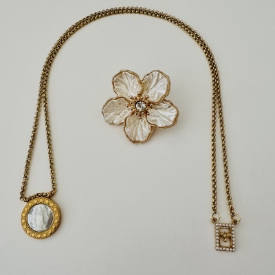 Colar dourado com pendente oval e adereço floral branco e dourado sobre fundo branco