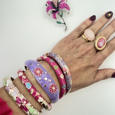 Mão com pulseiras e anéis florais coloridos e broche de flor lilás