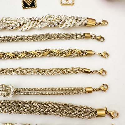 Pulseiras e brincos trançados dourados e prateados com fechos dourados sobre fundo branco.