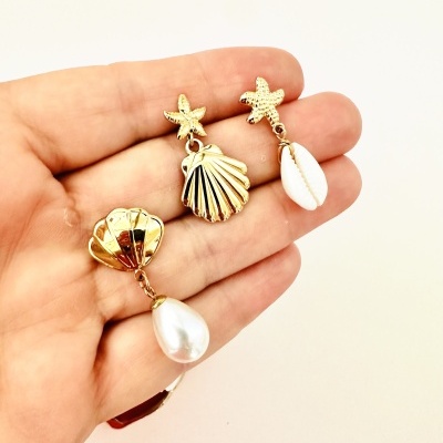 Brincos dourados com conchas e pérolas na mão