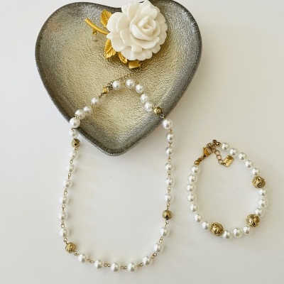 Colar e pulseira de pérolas com contas douradas em tigela coração cinzenta com flor decorativa branca