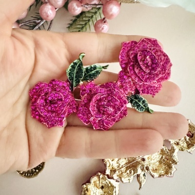Broche de rosas cor-de-rosa com pedraria e folhas verdes numa mão