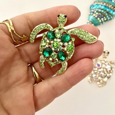 Broche tartaruga verde com pedras preciosas em mão feminina com anéis dourados