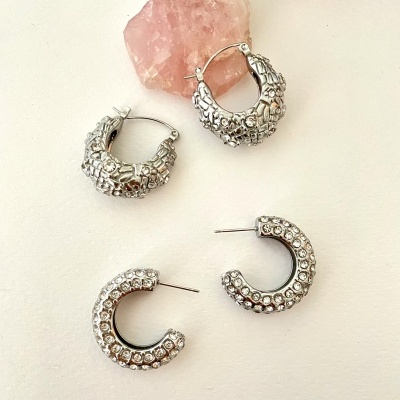 Dois pares de brincos prateados com texturas diferentes e cristal rosa ao fundo