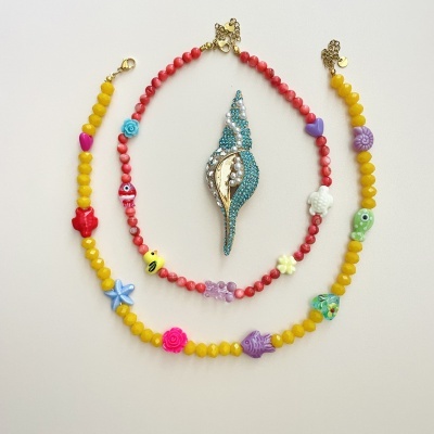 Colares coloridos com contas e pingentes variados, e broche azul com pérolas em forma de concha