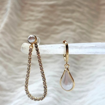 Par de brincos dourados com pedras brilhantes e pérola, design assimétrico.